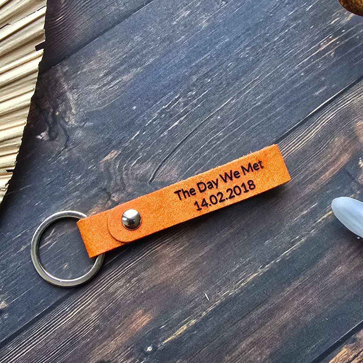 A personalized orange leather keychain with a metal split ring, engraved with 'The Day We Met 14.02.