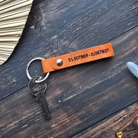 A personalized orange leather keychain with a silver key ring and keys, laid flat on a dark wood background with decorative props.
