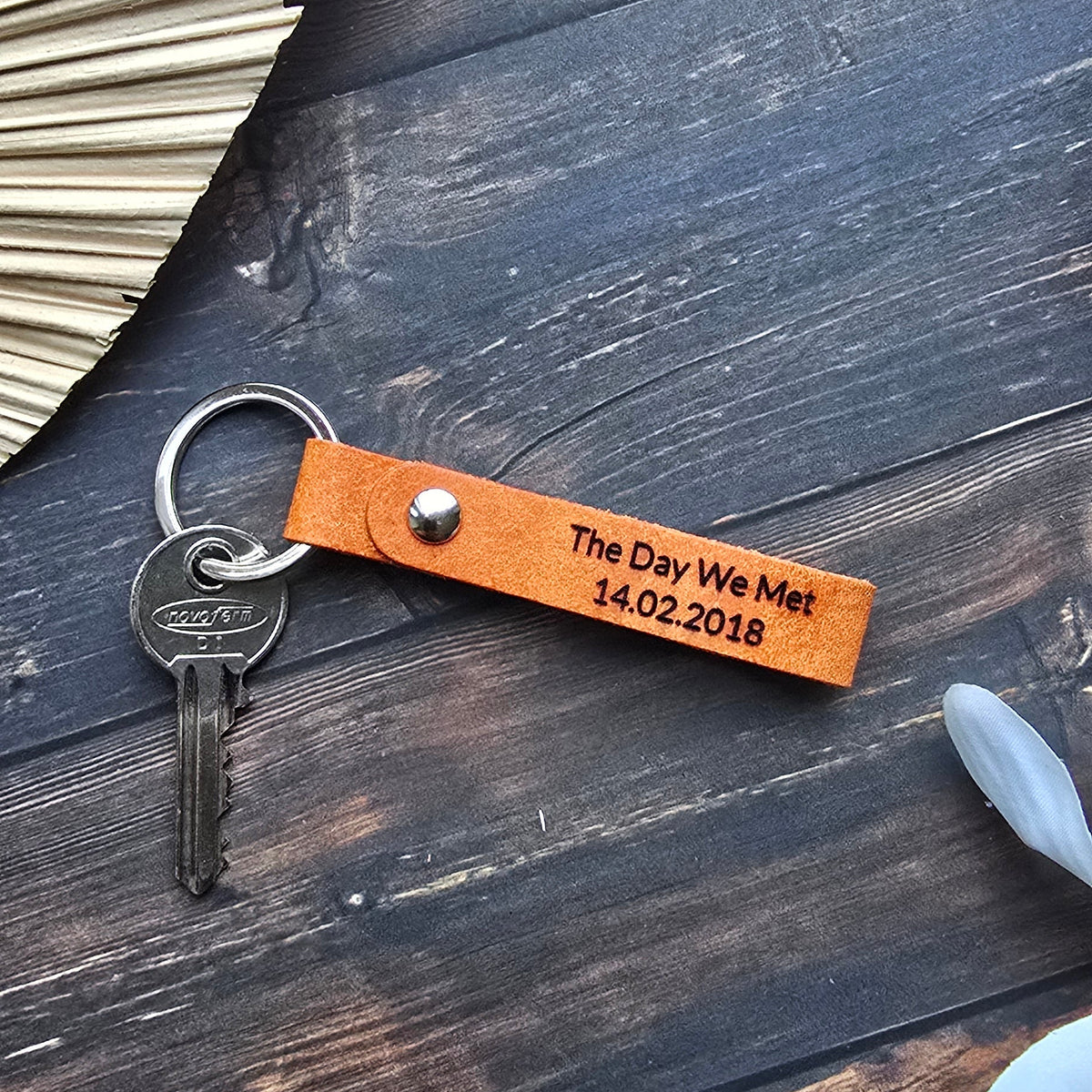 A personalized orange leather keychain with a metal key ring and key, laid flat on a dark wood background with decorative props.
