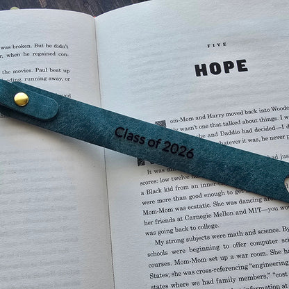 A teal metal bookmark with a gold button and engraved 'Class of 2026' text