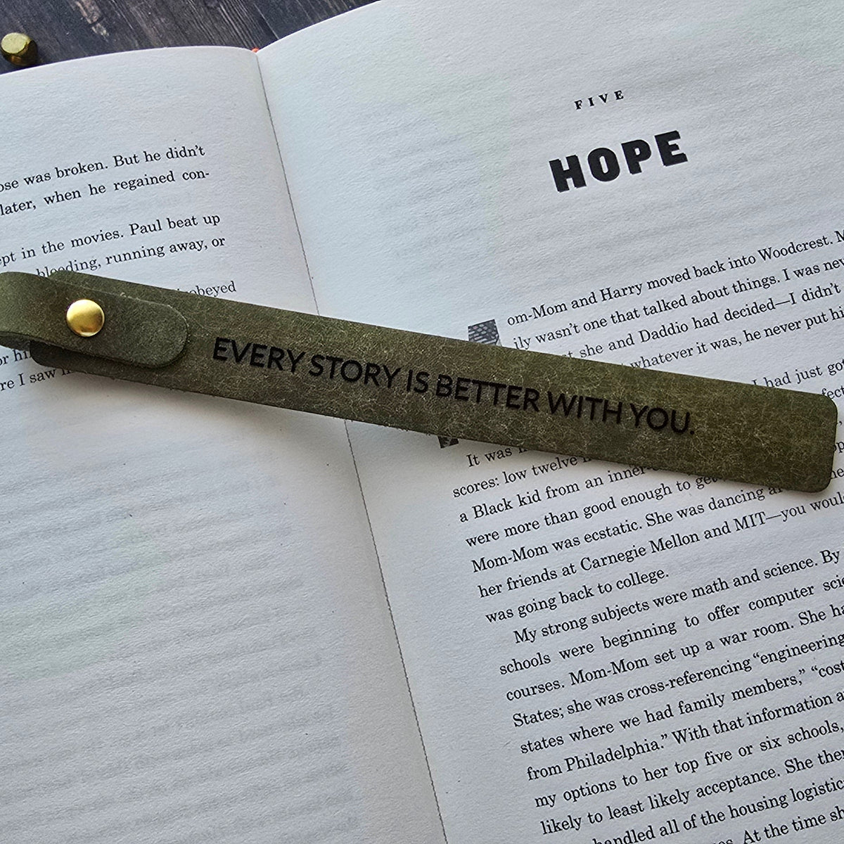 A leather bookmark with a gold rivet and the printed message 'EVERY STORY IS BETTER WITH YOU.