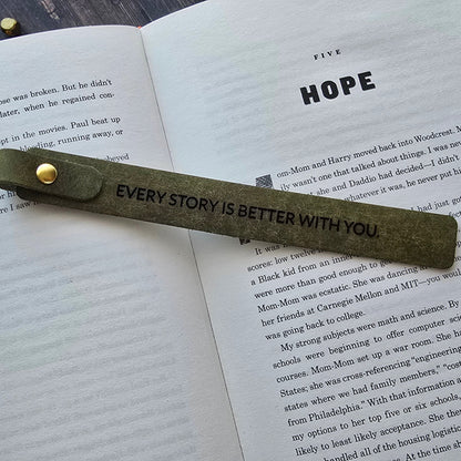 A leather bookmark with a gold rivet and the printed message 'EVERY STORY IS BETTER WITH YOU.