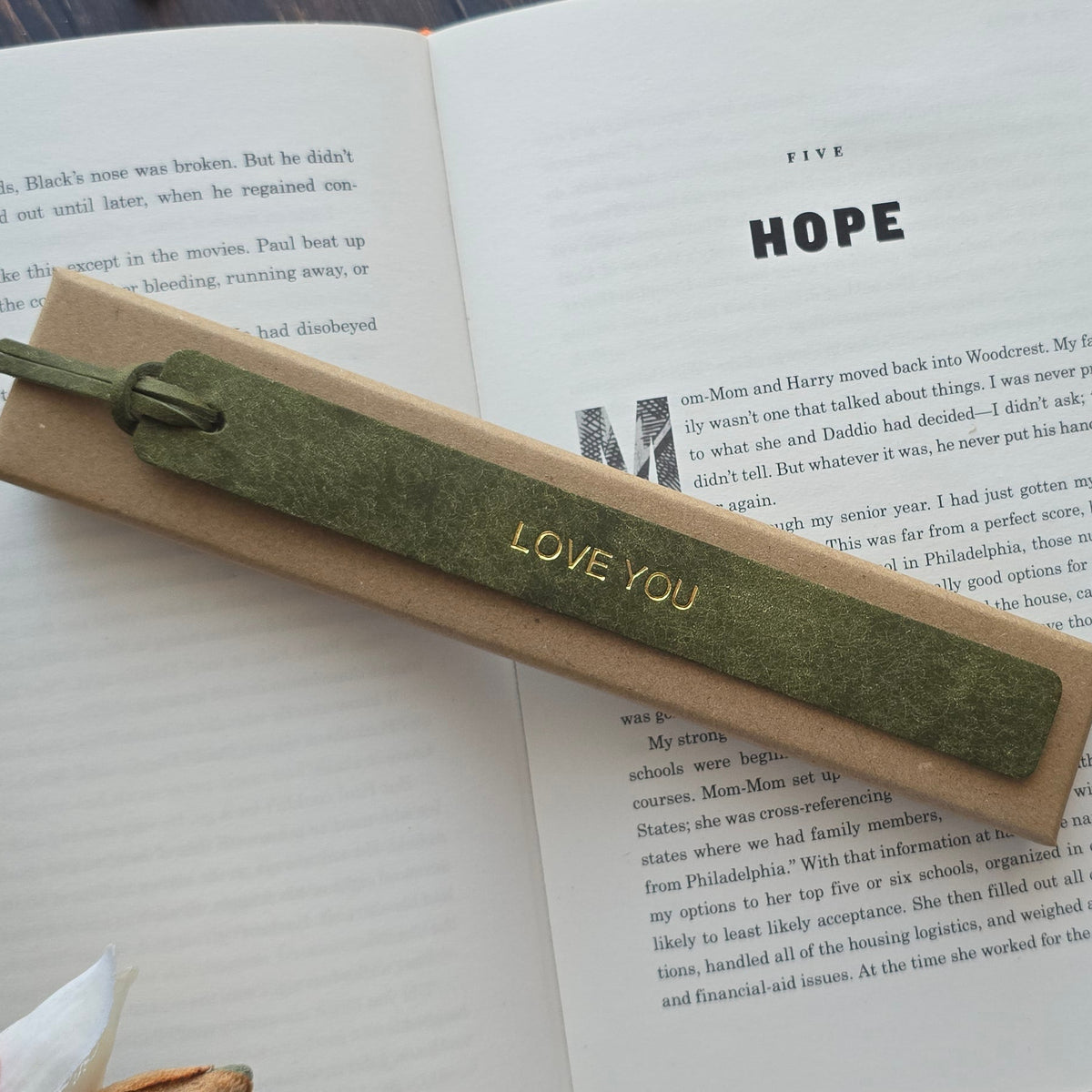 A green textured ribbon bookmark with 'LOVE YOU' printed in gold, resting on an open book.