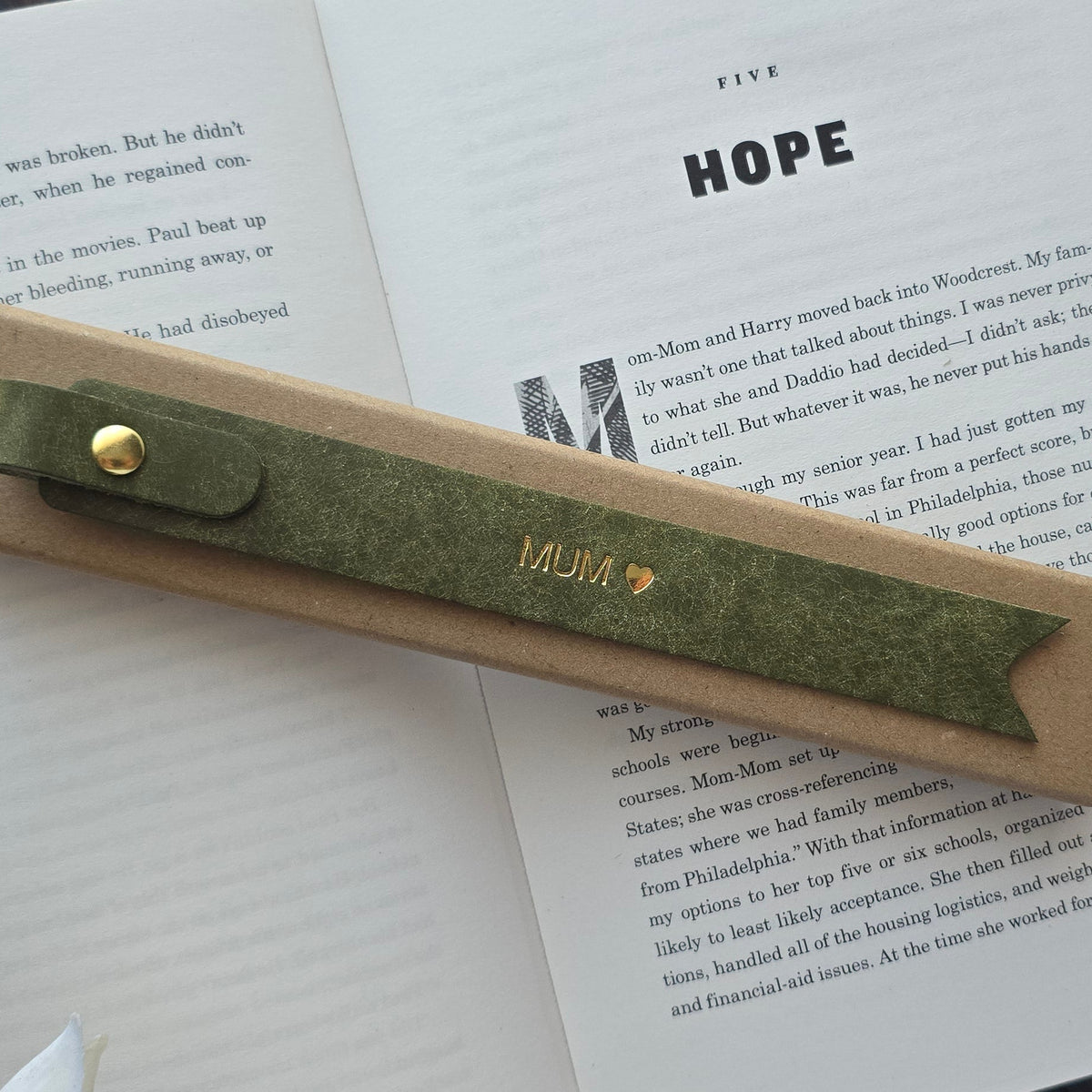An olive green leather bookmark with gold lettering reading